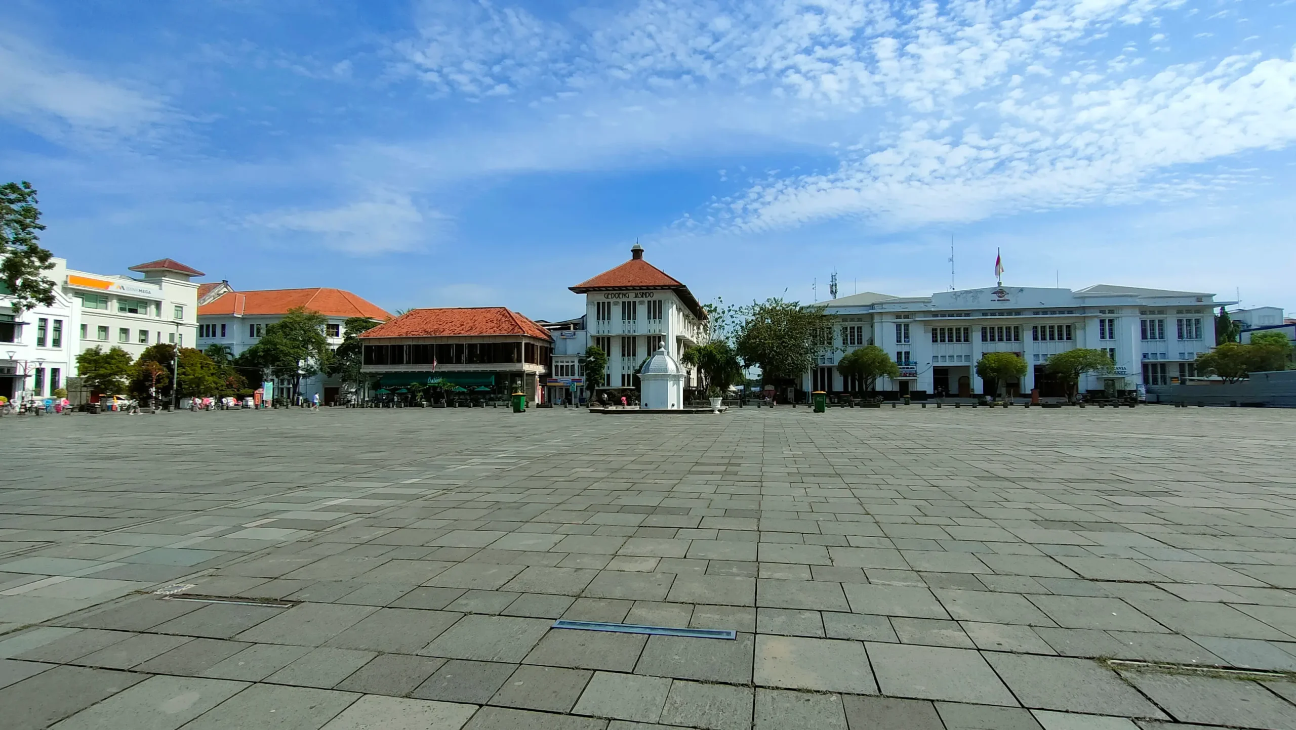 Pemandangan Taman Fatahillah di Kota Tua Jakarta dengan bangunan bersejarah dan langit biru cerah.