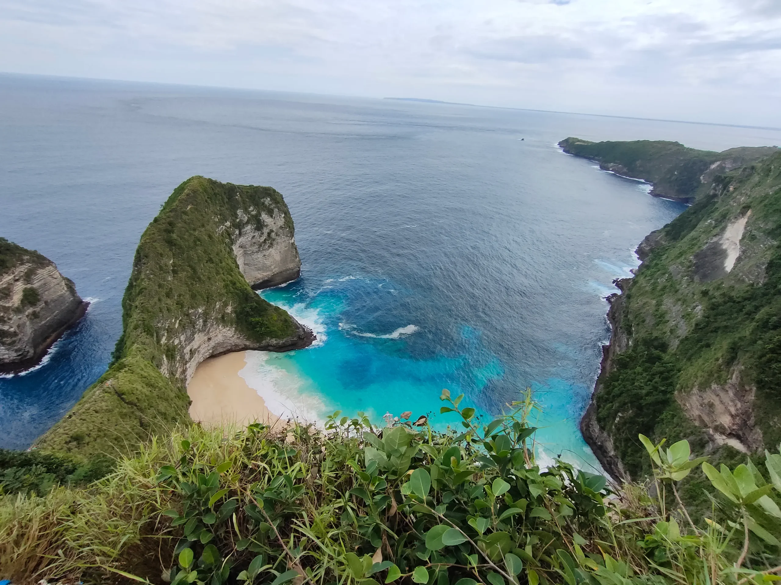 Pemandangan Pantai Kelingking di Nusa Penida, Bali dengan tebing karang, pasir putih, dan laut berwarna biru toska.